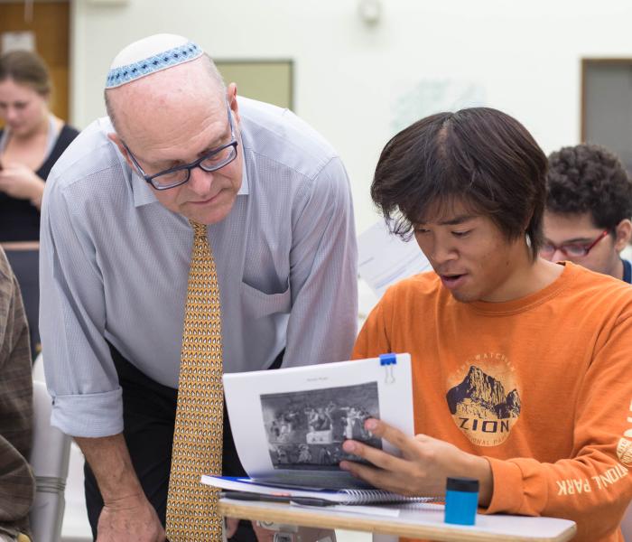 Faculty leaning over student answering questions and looking at a learning material