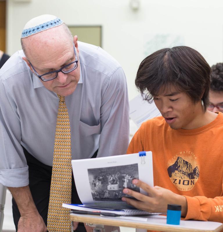 Faculty leaning over student answering questions and looking at a learning material